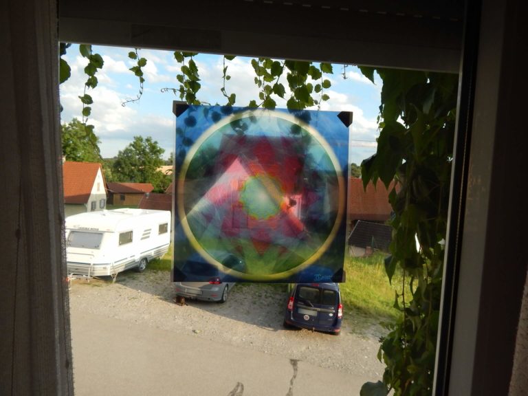 Foto von einem Fensterbild welches ein Mandala abbildet. Farben des Mandalas Rot, Blau, Gruen und Gelb