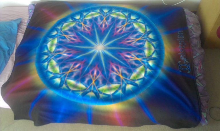 Mandala psychodelisch mit Strahlen und dark background auf einer Fleecedecke. Die Farbentiefe leuchtet einen an.