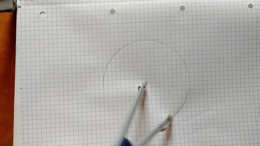 Bild von einem Karopapier und ein Zirkel, der einen Kreis macht. Anleitung: Einen Würfel zeichnen